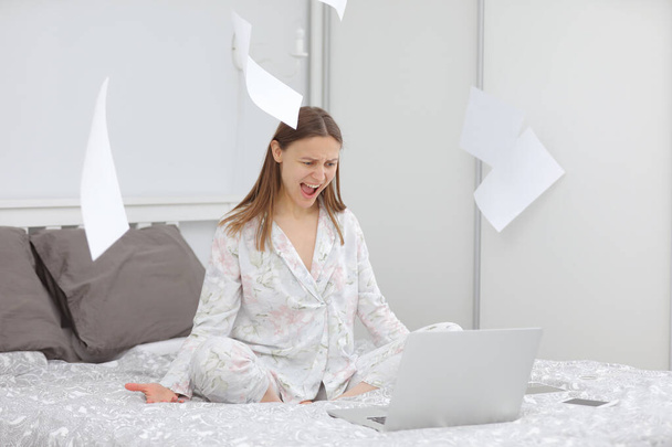 自宅で働いている疲れと怒りのビジネス女性。何か問題でも?。宿題だ。学習、ベッドの上のラップトップコンピュータを使用して。フリーランス。書く、タイプする。テクノロジーの概念。書類 - 写真・画像