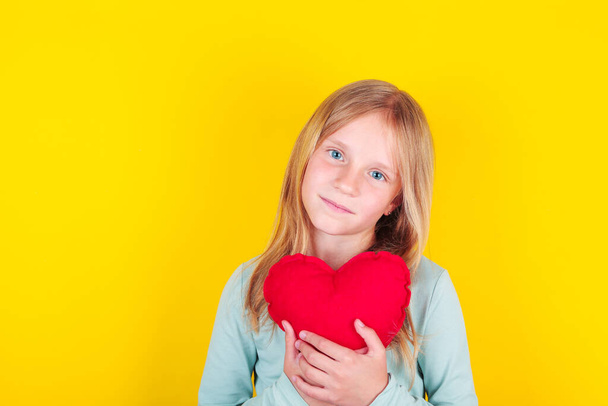 Mooi klein meisje met rood zacht hart, over gele achtergrond.  - Foto, afbeelding