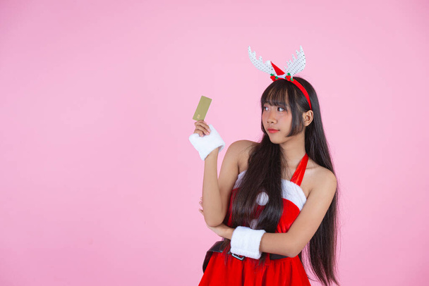 pretty girl in christmas costume holding credit card on pink background - Фото, изображение