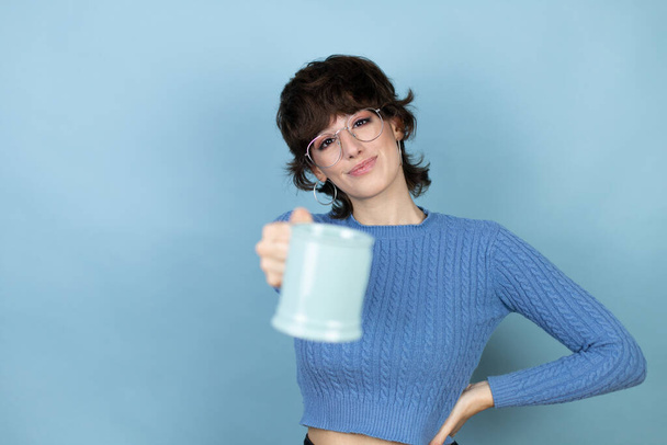 Joven mujer caucásica sobre fondo azul aislado disfrutando y bebiendo una taza de café - Foto, Imagen