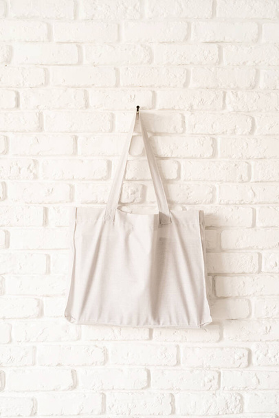 Falsa bolsa de tela de algodón blanco sobre fondo de pared de ladrillo blanco. Copiar espacio - Foto, Imagen