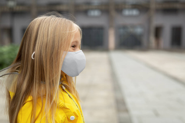 little caucasian girl 7 years old with blonde hair in yellow raincoat and face mask during Coronavirus pandemic. Colors of the year 2021 ultimate gray and illuminating - Foto, imagen