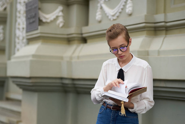 szczęśliwa studentka w pobliżu budynku z książką w ręku i okularami na twarzy - Zdjęcie, obraz