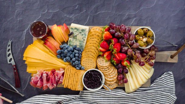 Plat gelegd. Het organiseren van gastronomische kaas, crakers, en fruit op een plank voor een grote kaasplank. - Foto, afbeelding