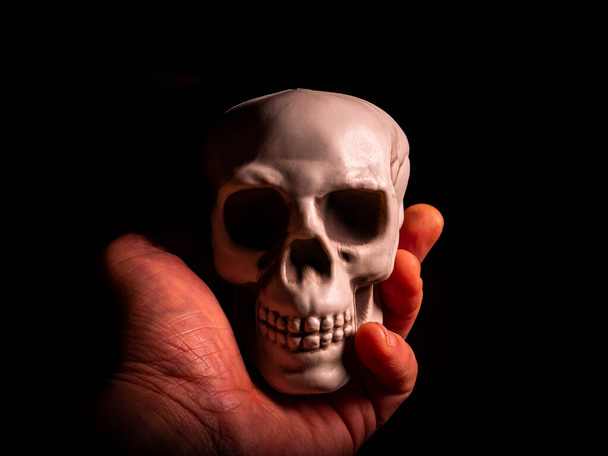 Human head skull in hand on black background. Halloween holiday. Human skull. Mans hand. All Saints Day. Halloween tradition. Festive masquerade. Religious celebration. Christian culture. Poster. - Zdjęcie, obraz