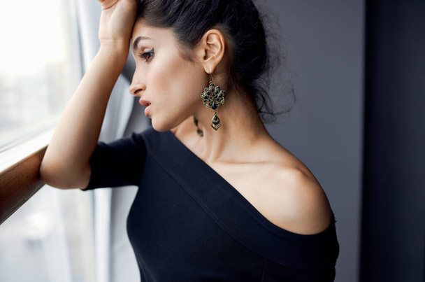 portrait of a beautiful woman in an evening dress near the window earrings hairstyle makeup model - Foto, Bild