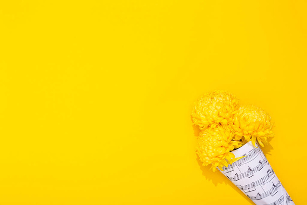 Bouquet of three lush chrysanthemums wrapped in a sheet with musical notes on yellow background. A holiday theme of music lovers. Happy Valentine Day February 14. Woman Day March 8. Mother Day May 8. - Foto, Imagen