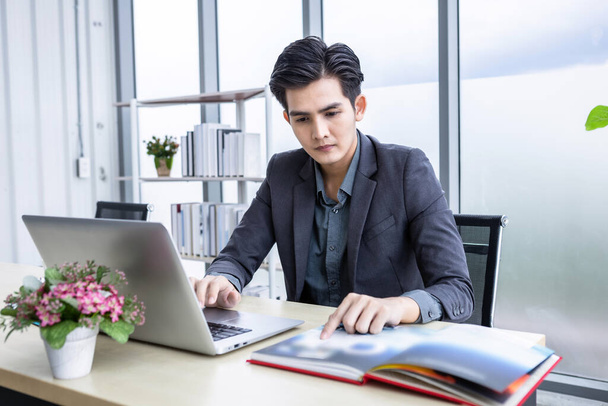 Happy of asian young businessman see a successful business plan on the laptop computer and Catalog Design on wooden table background in office,business expressed confidence embolden - Фото, изображение