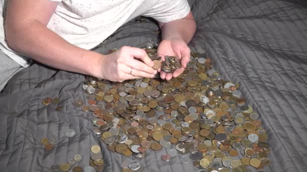 ένα άτομο επιλέγει από ένα σωρό νομίσματα από διαφορετικές χώρες. Ξαπλώνει στον καναπέ - Πλάνα, βίντεο