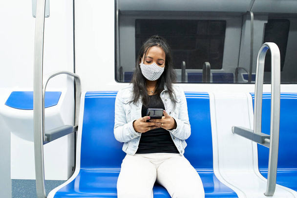 Чорна жінка сидить на самоті в машині метро за допомогою смартфона. Афроамериканська дівчина розмовляє та спілкується в Інтернеті на громадському транспорті.. - Фото, зображення