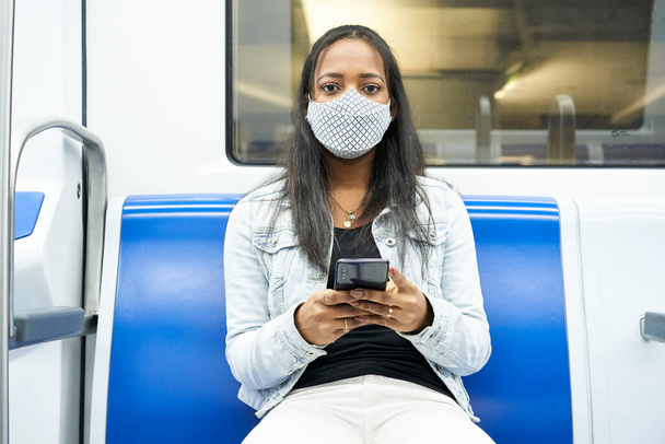 Foto en medio de una mujer negra sentada en el vagón del metro mirando a una cámara con un smartphone. - Foto, Imagen