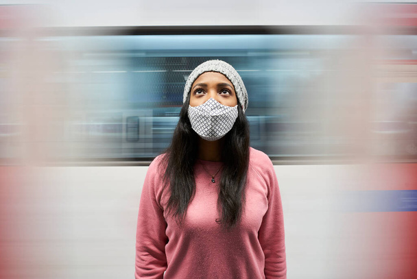 Metro peronunda kameranın önünde maske takmış genç bir kadının portresi. Arka planda metro kervanı hareketi. - Fotoğraf, Görsel
