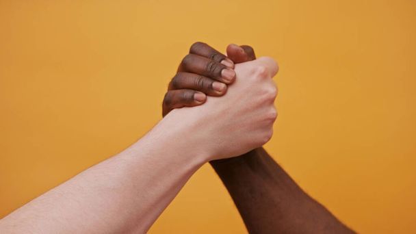 чорно-білі руки, що тримаються разом, ізольовані на помаранчевому фоні. крупним планом
 - Фото, зображення