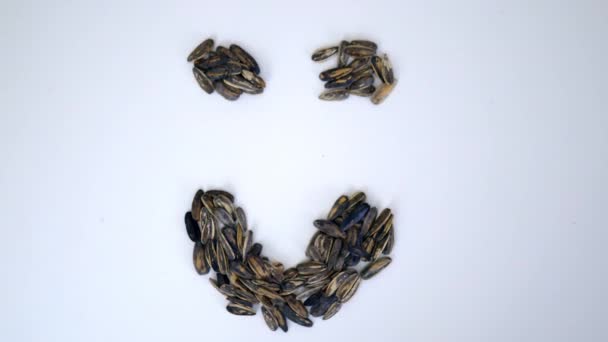 Petite pile de graines de tournesol en forme de visage souriant sur une table blanche - Séquence, vidéo