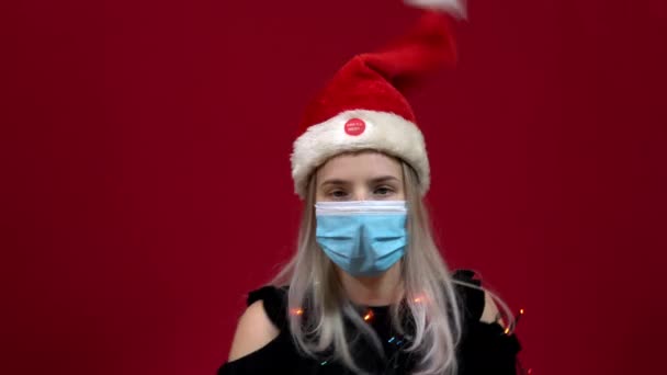 Mujer con máscara médica cantando y bailando junto con un sombrero de Navidad bailando en vivo en su cabeza - Imágenes, Vídeo