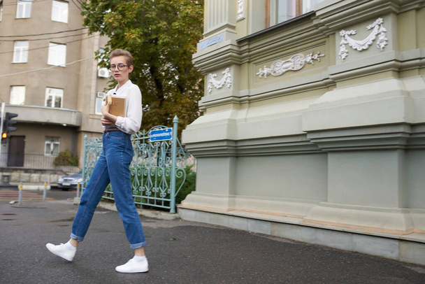 красивые женские джинсы модели с книгой в руке рядом со зданием на улице - Фото, изображение