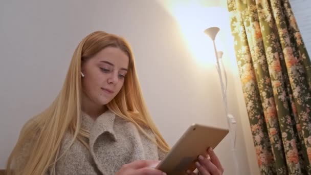 Boldog mosolygós fiatal nő ül a kanapén, barát a videón hívás tablet - Felvétel, videó