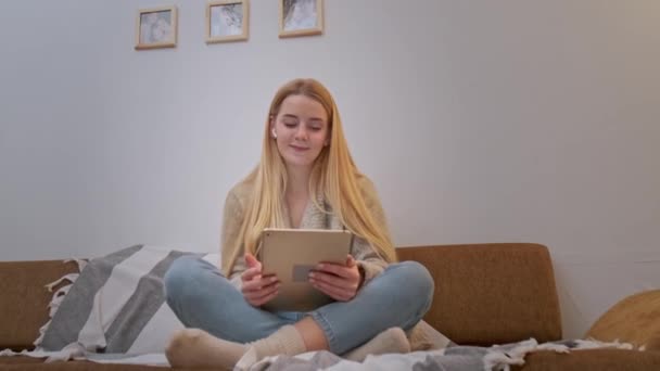 Nuori nainen istuu sohvalla ja web surfing ja tanssia digitaalinen tabletti. - Materiaali, video