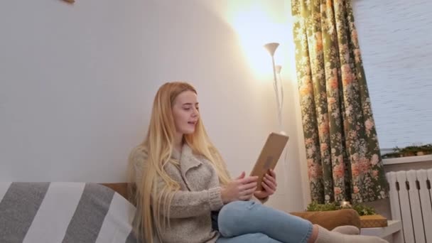 Szczęśliwy uśmiech młoda kobieta siedzi na kanapie, przyjaciel na wideo rozmowy za pomocą tabletu - Materiał filmowy, wideo