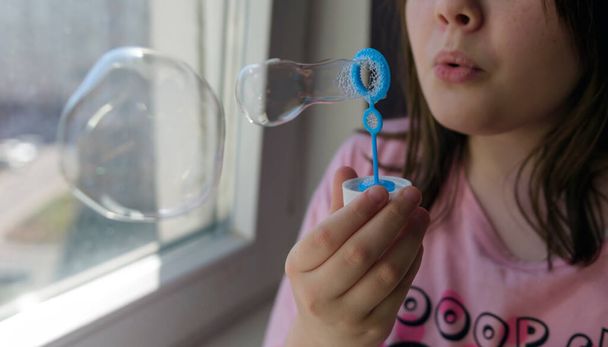 La niña sopla burbujas de jabón en el apartamento. Autoaislamiento durante el coronavirus. - Foto, Imagen