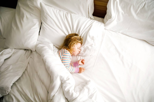 Mignon petit tout-petit fille qui dort dans un grand lit de parents. Adorable bébé enfant rêvant dans un lit d'hôtel en vacances en famille ou à la maison. - Photo, image