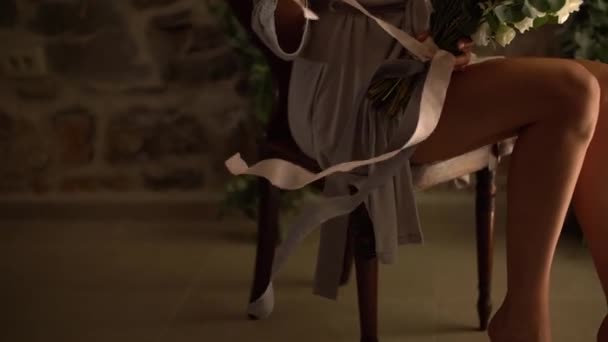 Una mujer con una túnica de seda sostiene un ramo de novia en su regazo y juega con cintas largas - Imágenes, Vídeo