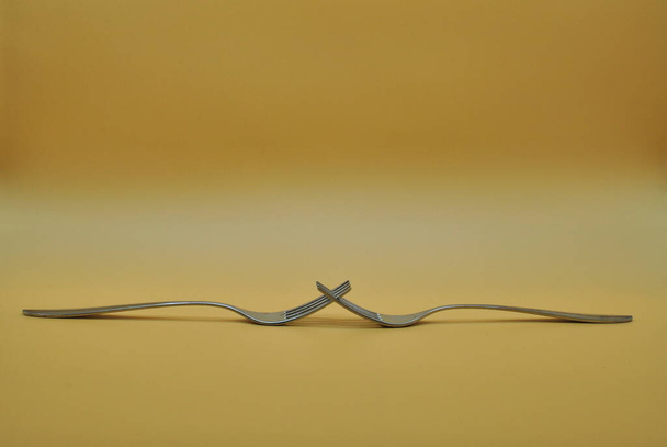 composition of 2 intertwined forks isolated over neutral orange background - Fotoğraf, Görsel
