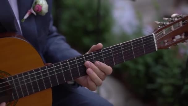 Mężczyzna w garniturze z butonierką gra na gitarze akustycznej - Materiał filmowy, wideo