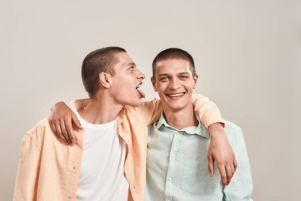 Portrait of two young twin brothers hugging and having fun while posing together isolated over beige background - Fotografie, Obrázek