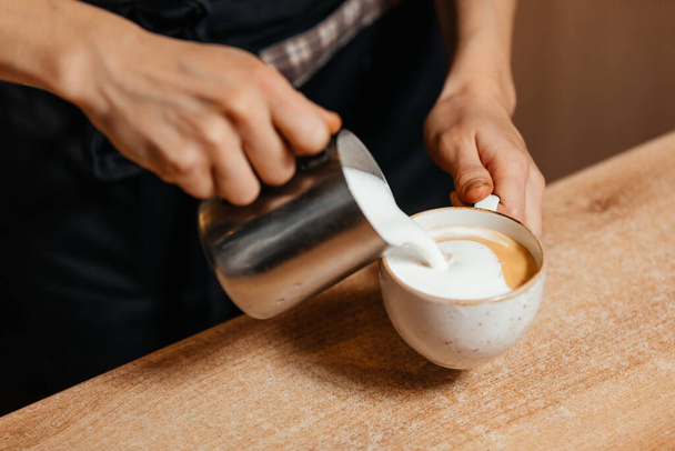 Baristas hands pour hot milk into an espresso cup. Cooking a cappuccino. - Photo, Image