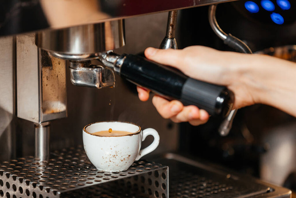 Baristas χέρι ρίχνει ζυθοποιηθεί φρέσκο καφέ από τη μηχανή του καφέ σε ένα λευκό κύπελλο - Φωτογραφία, εικόνα