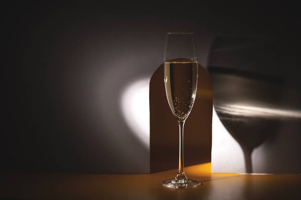 Stylish glass of champagne in hard light with creative shadows - Фото, изображение