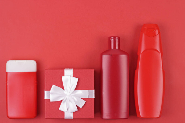 Christmas sale of beauty products concept. Blank red cosmetics bottles and Christmas gift on red background.Top view with place for text. - Φωτογραφία, εικόνα