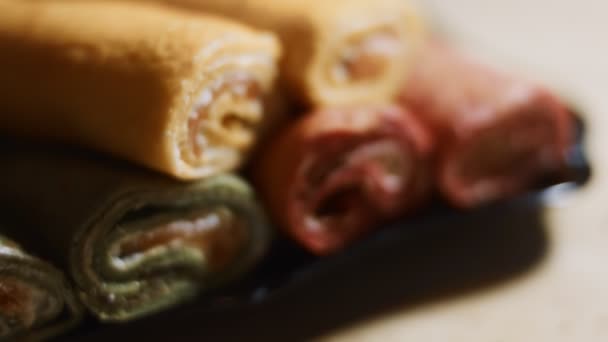 Minces crêpes colorées savoureuses. Macro vue des crêpes roulées rouges, jaunes et vertes coupées avec fromage à la crème et garniture de saumon sur un plat. Vidéo 4K. Mouvement lent - Séquence, vidéo