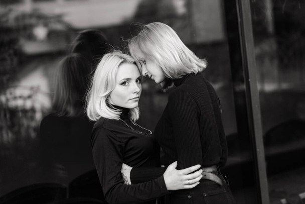 Zwei junge Frauen gehen lächelnd und umarmen und küssen sich im Freien - Foto, Bild