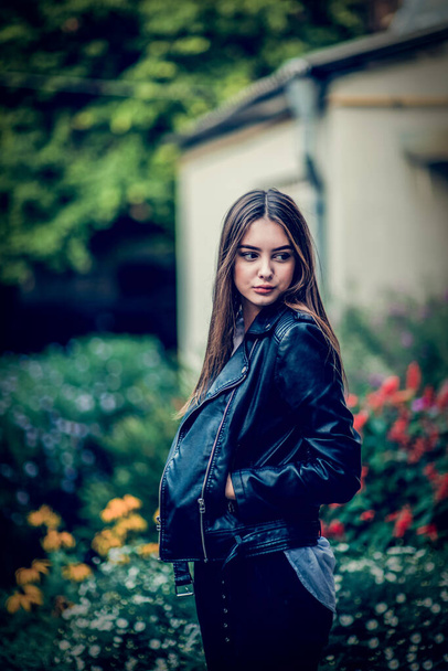 young girl in a black leather jacket stands. A series of photos with a beautiful brunette outdoors. - Photo, Image