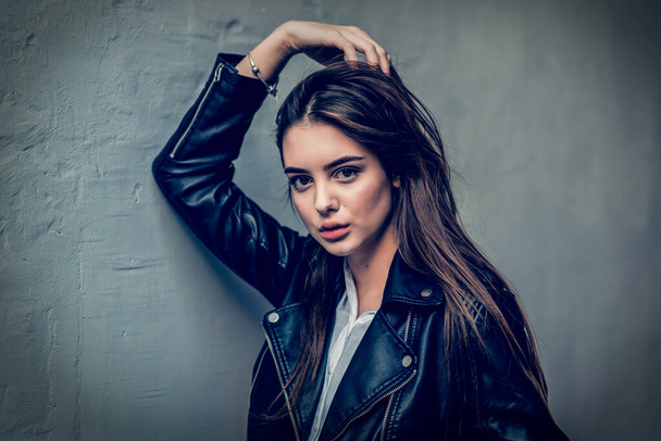young girl in a black leather jacket stands. A series of photos with a beautiful brunette outdoors. - Фото, зображення