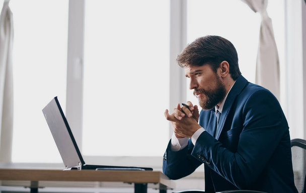 Озадаченный бизнесмен смотрит на ноутбук за столом офисной модели - Фото, изображение