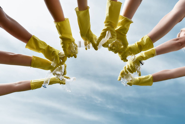 Clean up day. Group of volunteers or eco activists wearing yellow protective rubber gloves holding plastic bottles against blue sky. - Fotoğraf, Görsel