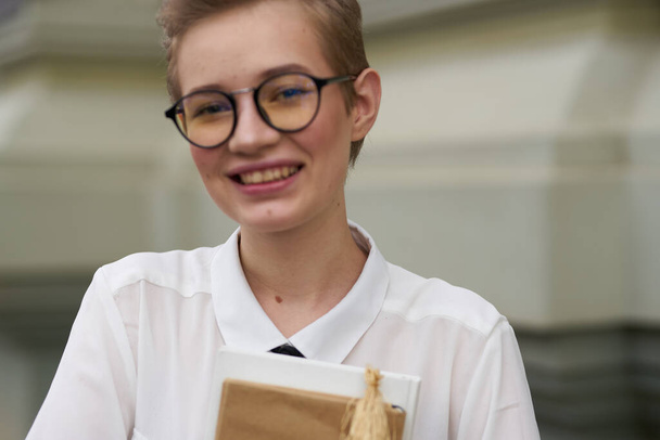 happy female student near the building with a book in hand and glasses on her face - Fotografie, Obrázek