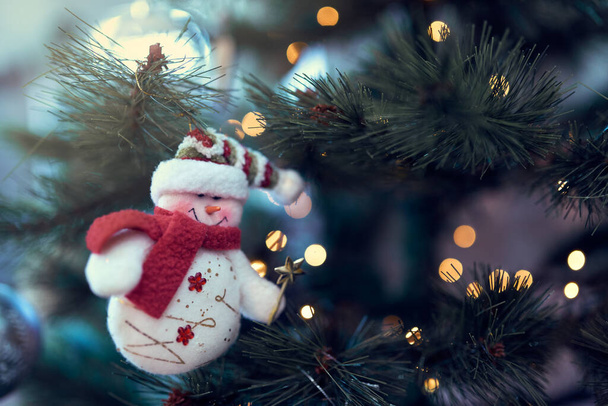 primer plano de muñeco de nieve colgando en el árbol de Navidad con luces encendidas - Foto, imagen