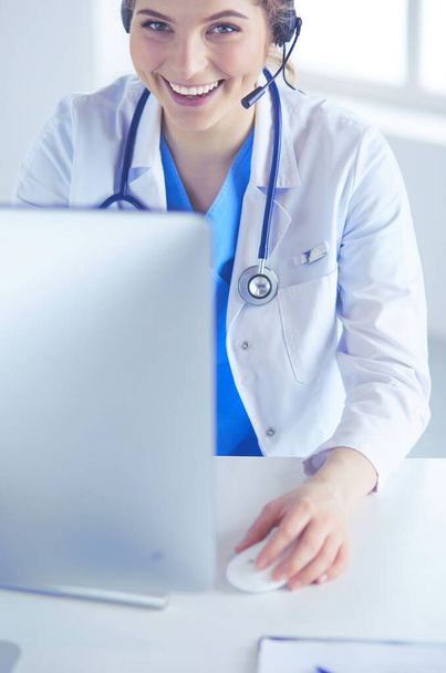 Doctor wearing headset sitting behind a desk with laptop - Фото, зображення