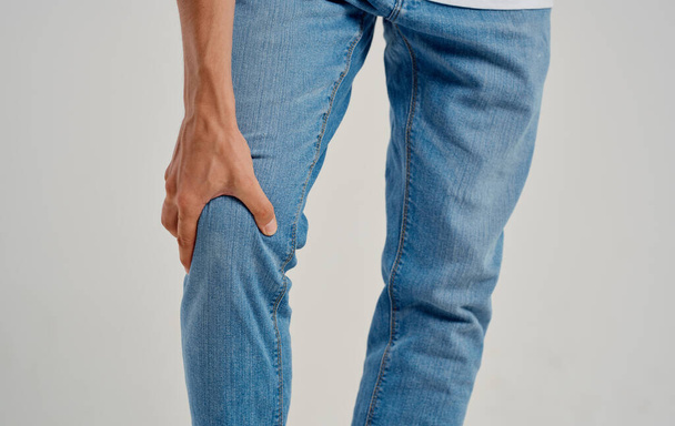 mężczyzna w dżinsach dotyka kolana dłońmi na jasnym tle przycięty widok - Zdjęcie, obraz