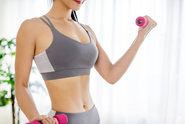  mujer joven en ropa deportiva haciendo ejercicios de fitness con mancuerna y mostrando abdominales - Foto, Imagen