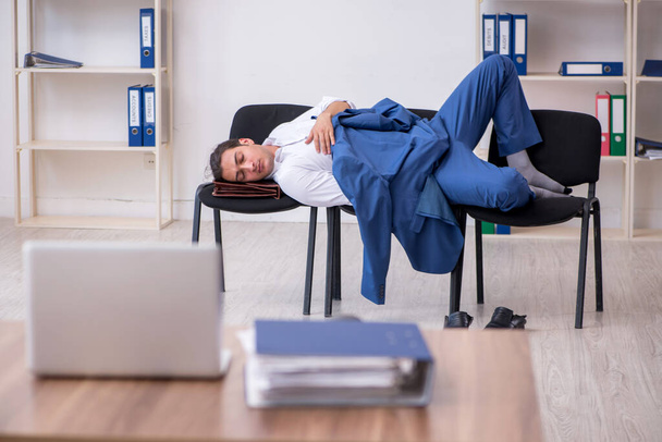 Nuori miespuolinen työntekijä nukkuu toimistossa tuoleilla - Valokuva, kuva