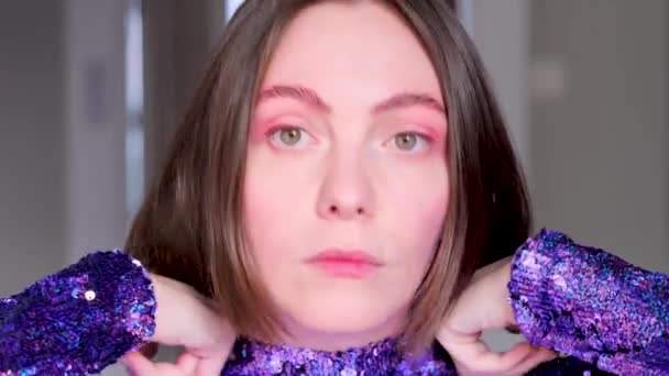 Mujer ajusta vestido púrpura y peinado corto cerca del espejo - Imágenes, Vídeo