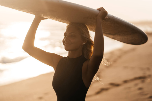 Beautiful surfer woman on the beach at sunset - Фото, зображення