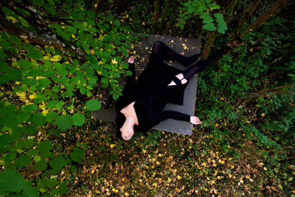 セクシーな若いブルネットの女性は、落葉樹の秋の森の正方形のテーブルの上の黒いドレスに横たわって、スペースをコピー - 写真・画像