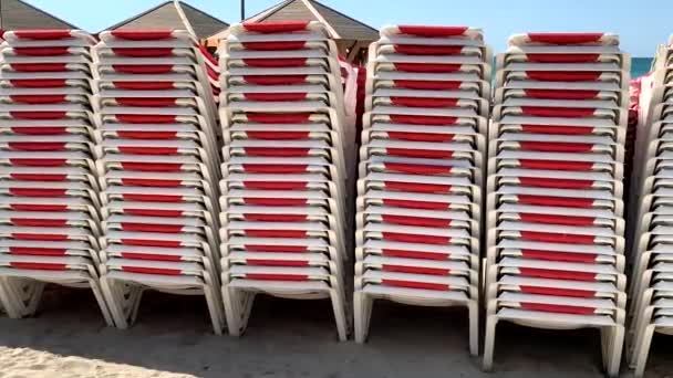 Красно-белые солнцезащитные кресла сложены на песчаном пляже, пустой пляж с песчаными пляжами. 4K - Кадры, видео