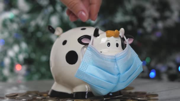 Piggy τράπεζα ειδώλιο με τη μορφή αγελάδας ή ταύρου σε ιατρική μάσκα. Ο αντίκτυπος της πανδημίας στην οικονομία. Χέρια με ένα κουμπαρά από κοντά - Πλάνα, βίντεο